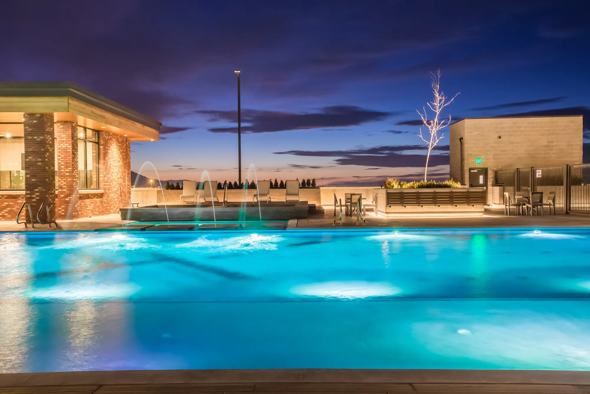 The 4th West rooftop pool lit and glowing at dusk, fountains on, skyline beyond