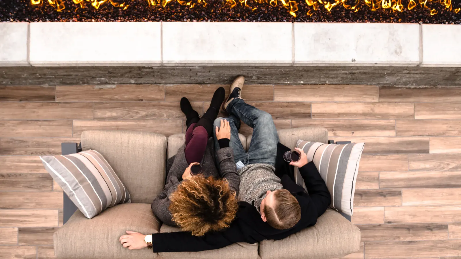 Two people on a rooftop sofa beside the fire, read from above