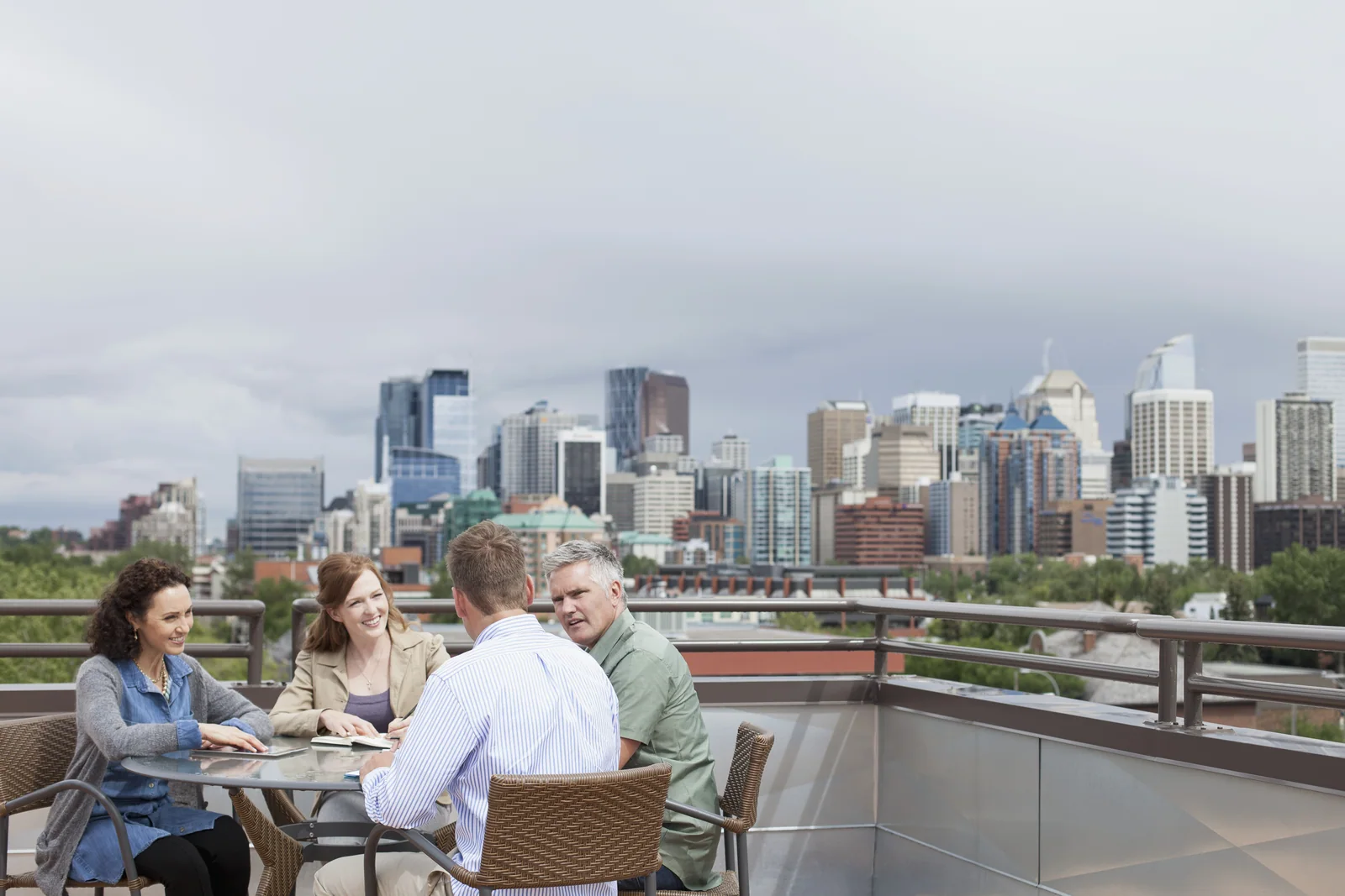 Two men and two women holding a business meeting on a rooftop patio with the city skyline in the background