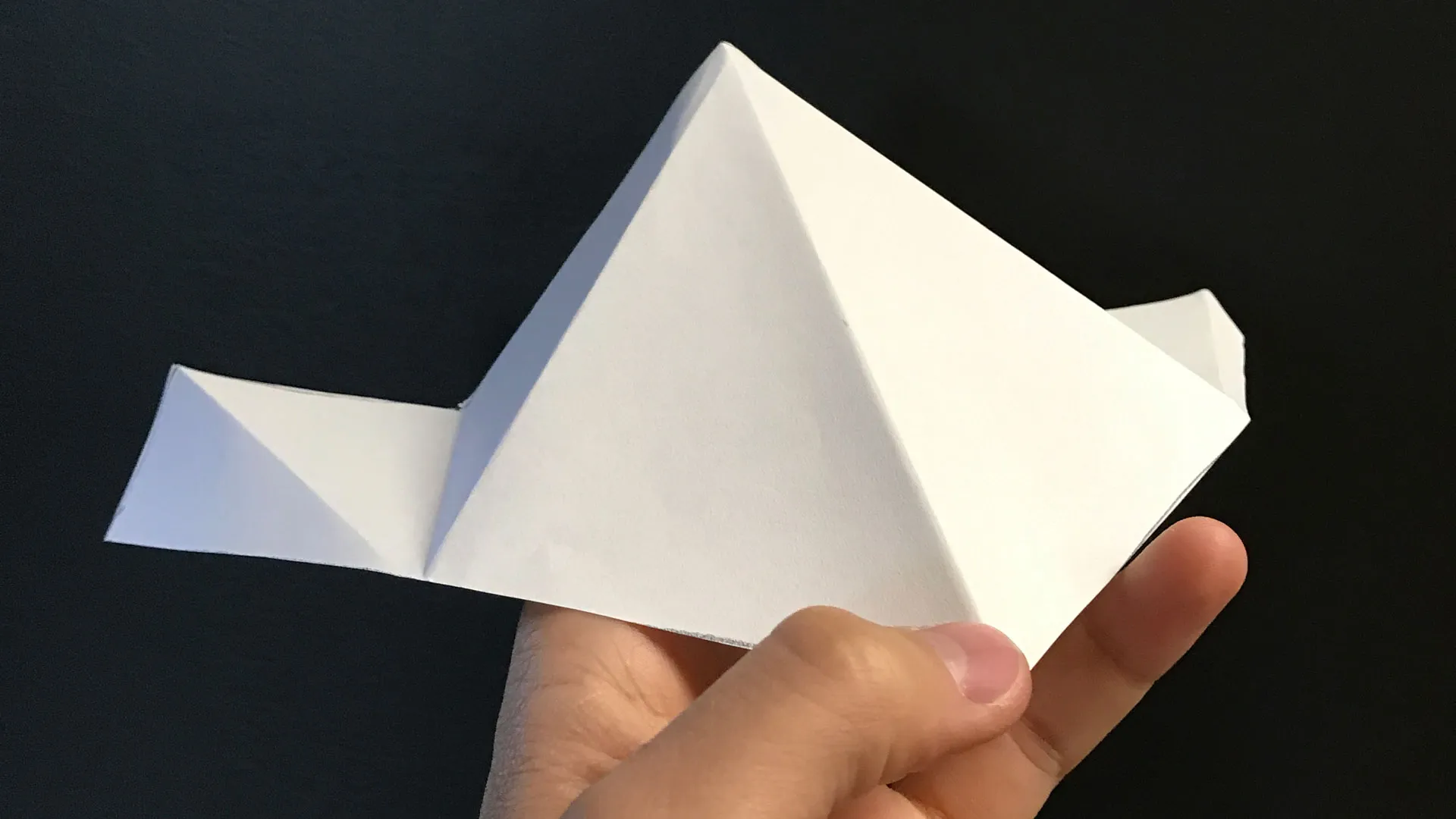 A folded paper model of the shade structure held in one hand