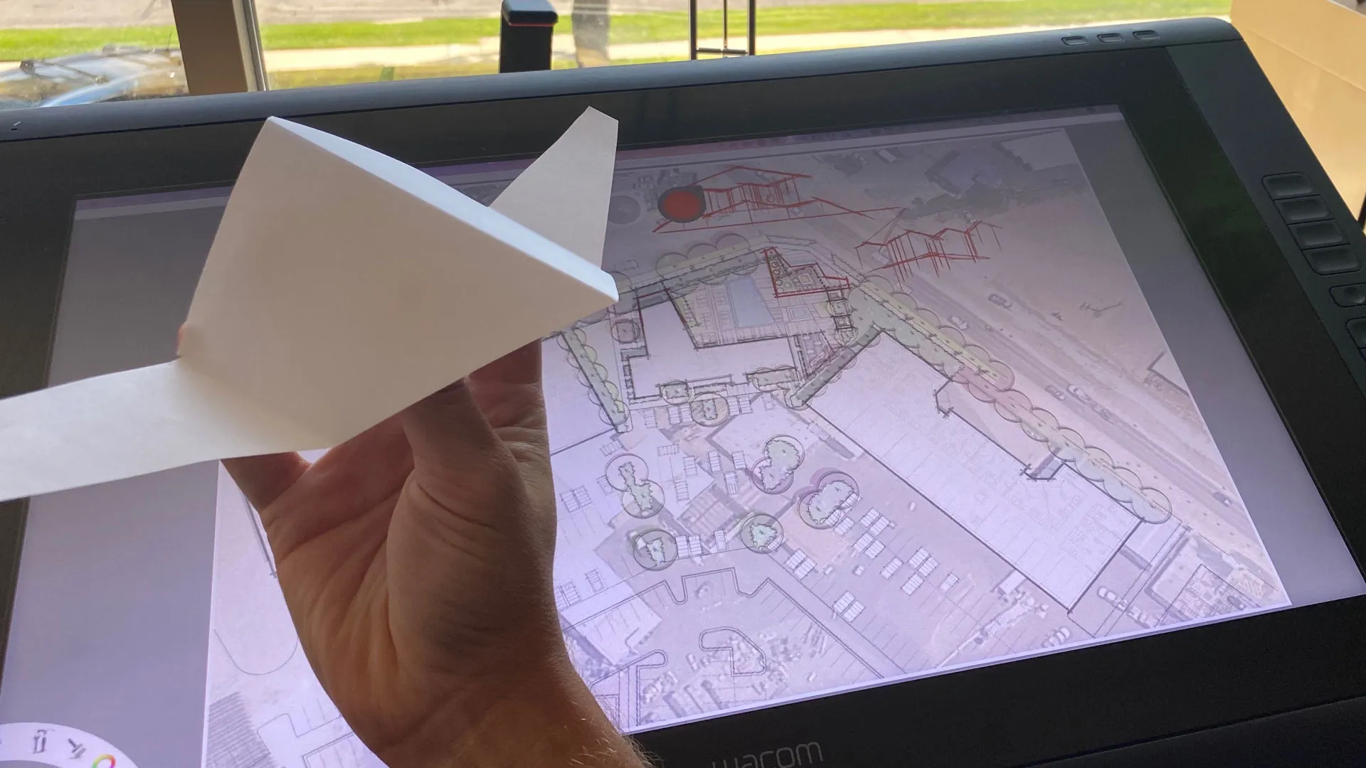 The folded paper model held over the digital site plan on a screen