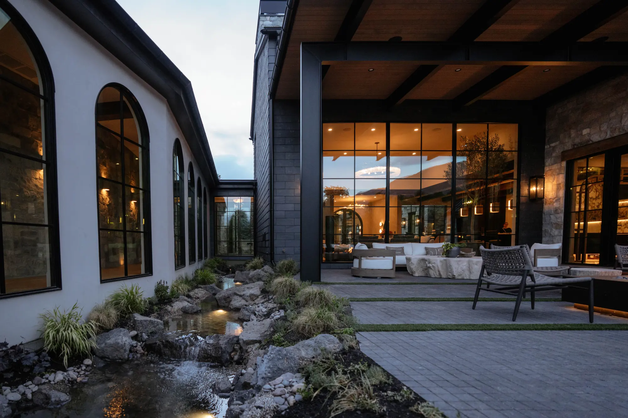 The lit creek running past the arched windows to the covered patio at dusk