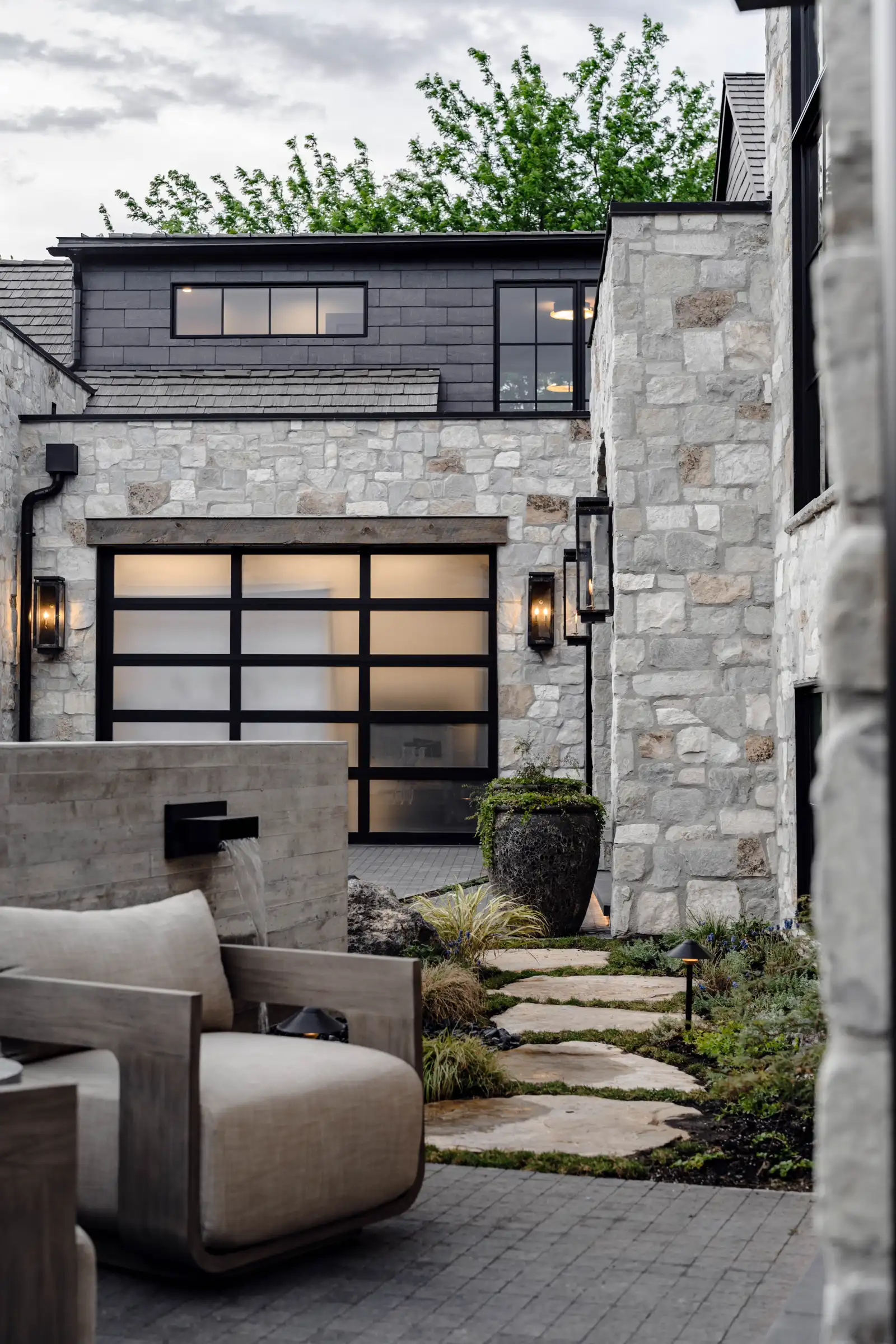 A lounge chair beside a scupper and stepping stones through layered planting in the entry courtyard