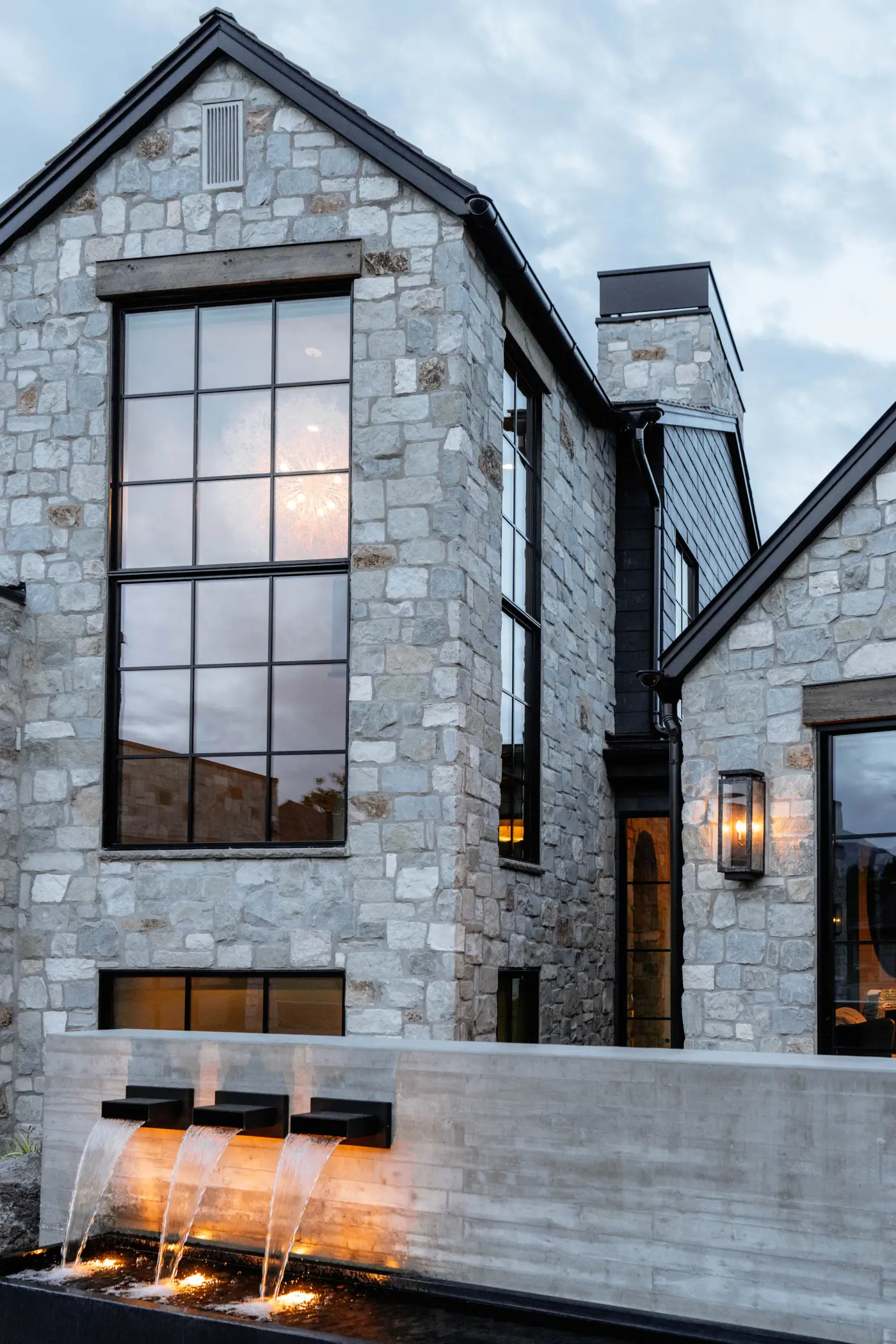 Hidden Oak Haus stone gable at dusk with the lit water wall scuppers below