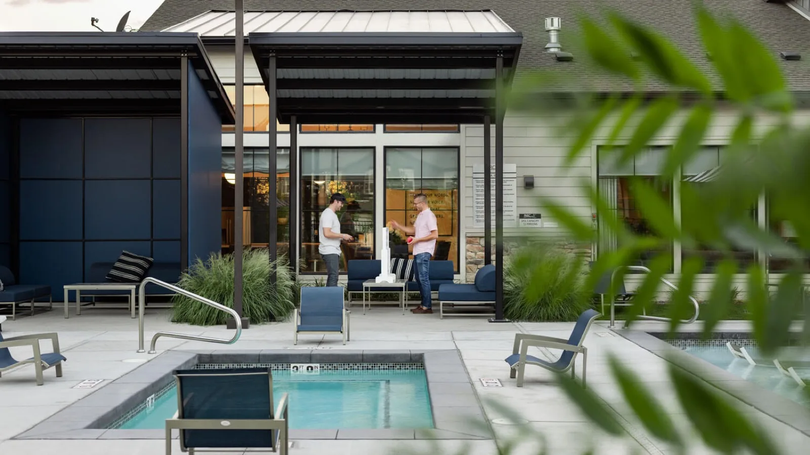 The Parc on 5th spa and pool deck at ground level, two people talking under the steel pergola by the clubhouse