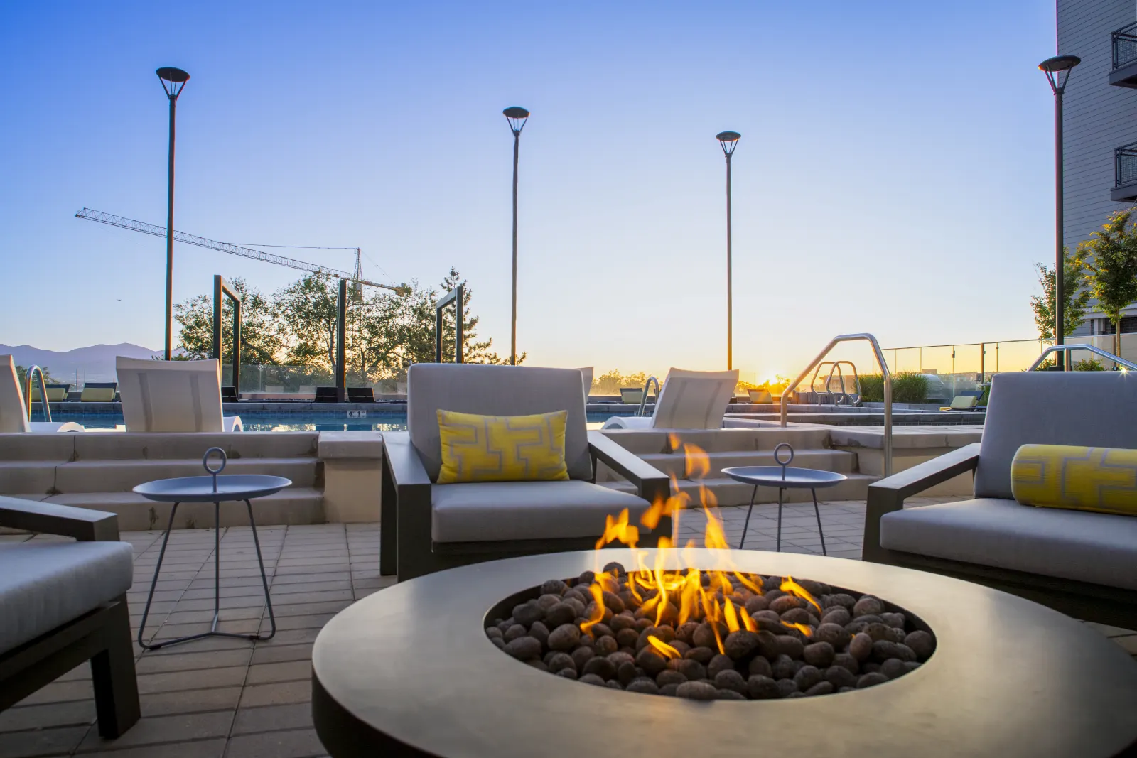 A lit fire pit on the pool terrace at sunset, lounge seating around it and the pool behind