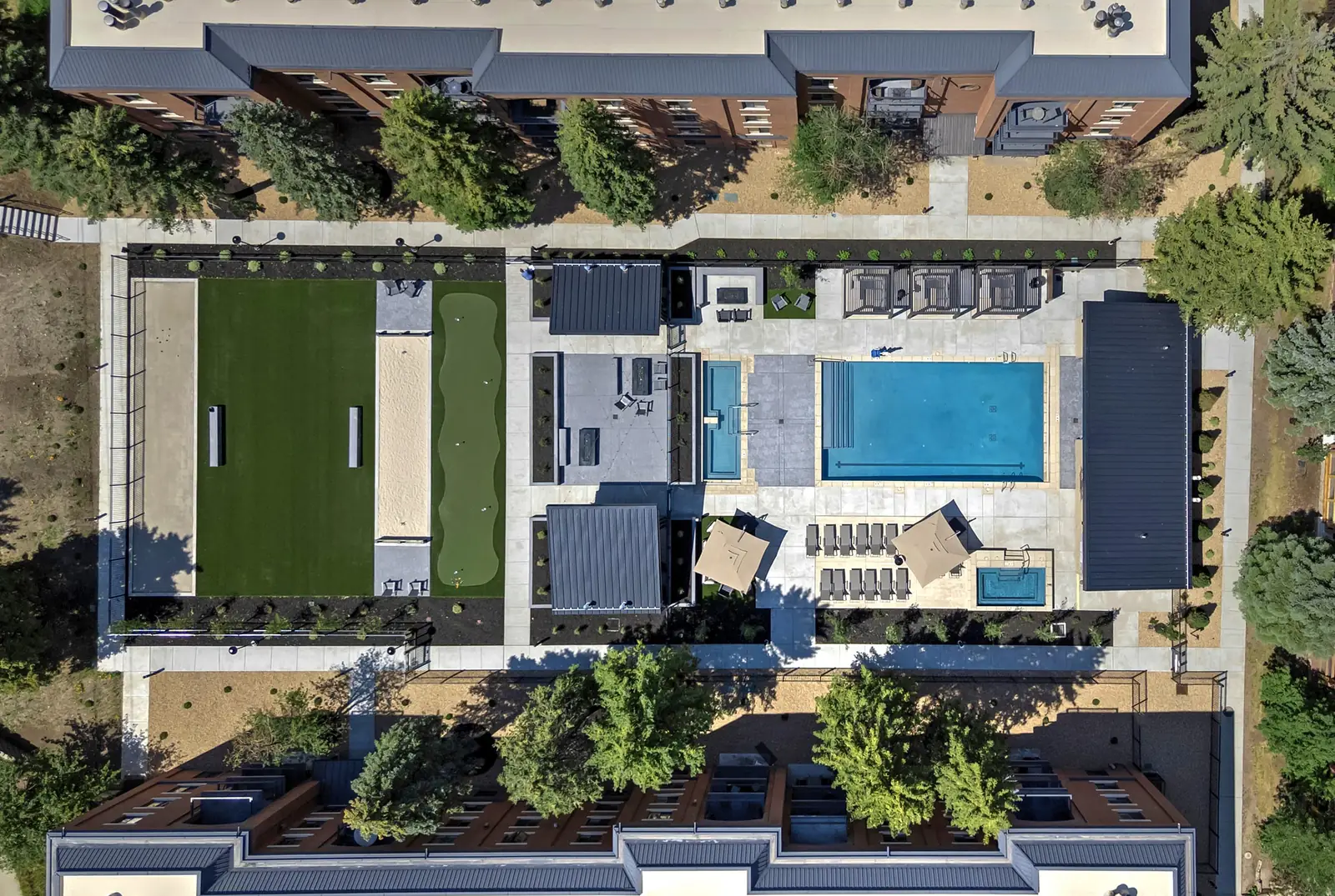 Straight-down aerial of the whole amenity area between two condo buildings: lawn and bocce court, putting green, covered pavilions, pools, hot tubs and cabanas