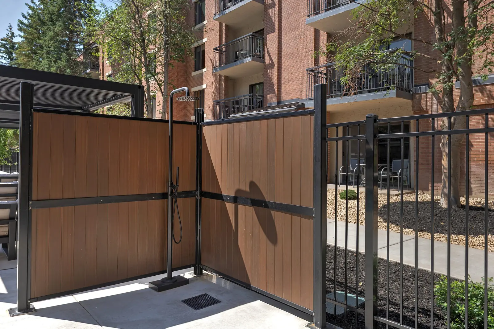 Outdoor shower behind wood-look screen panels, black metal fencing alongside