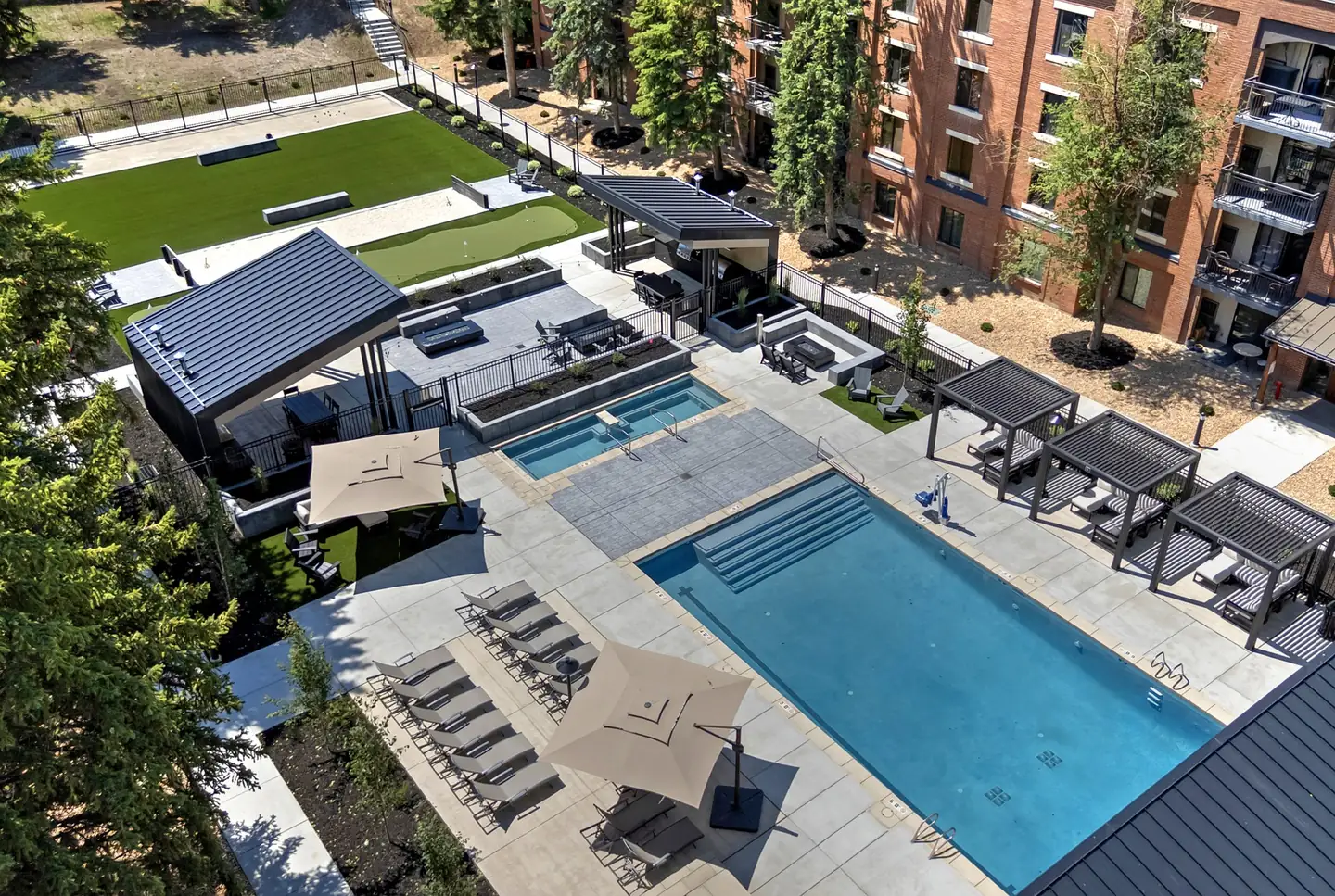 Aerial of the pool and hot tub with lounge chairs and shade cabanas, the lawn and putting green beyond