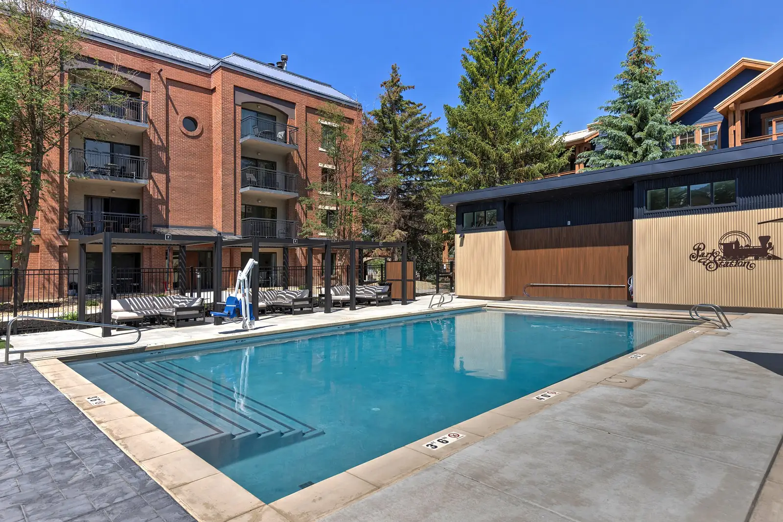 The pool by day, lounge chairs under shade pergolas and the Park Station sign on the pool building