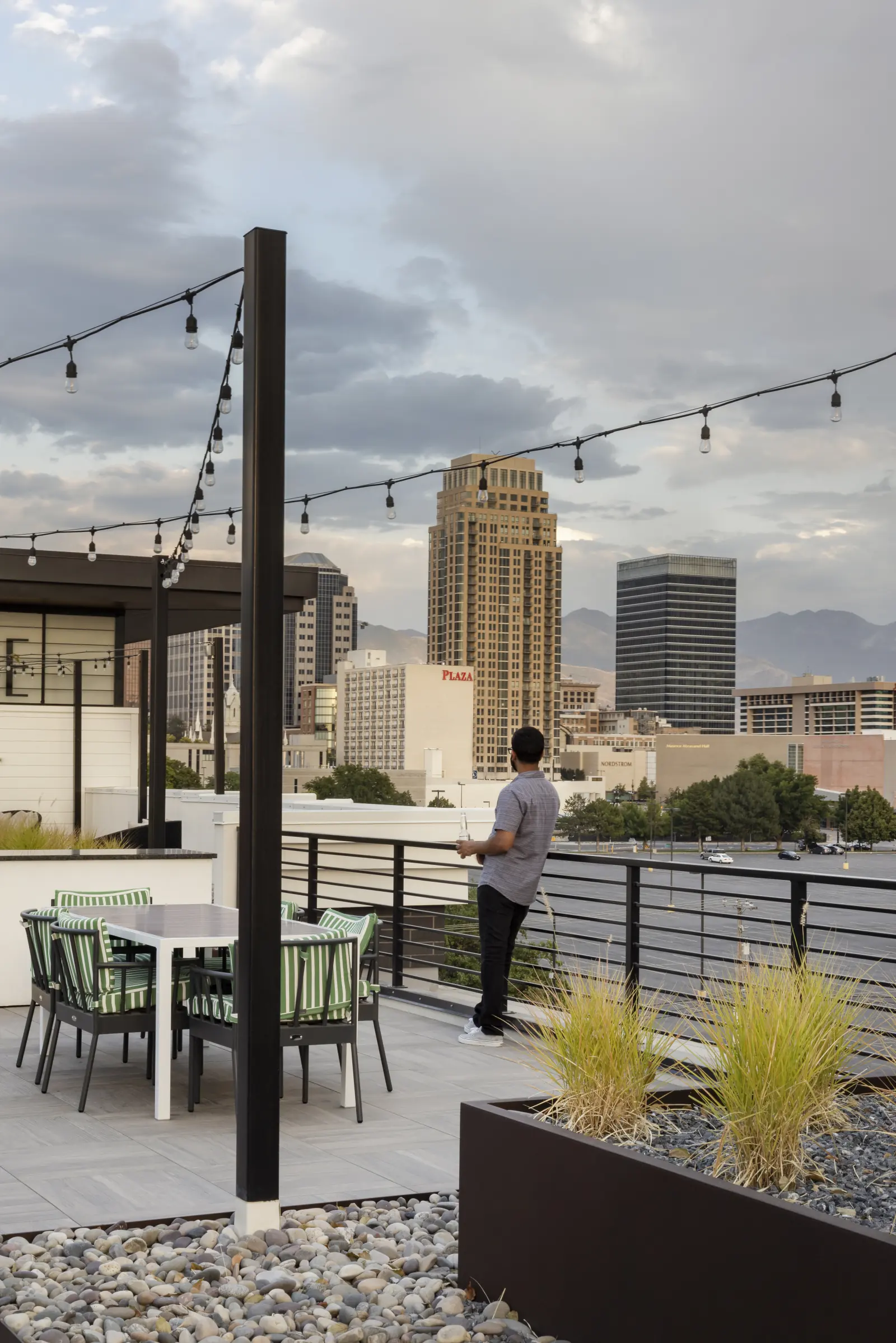 A resident at the rooftop edge under string lights, the skyline beyond