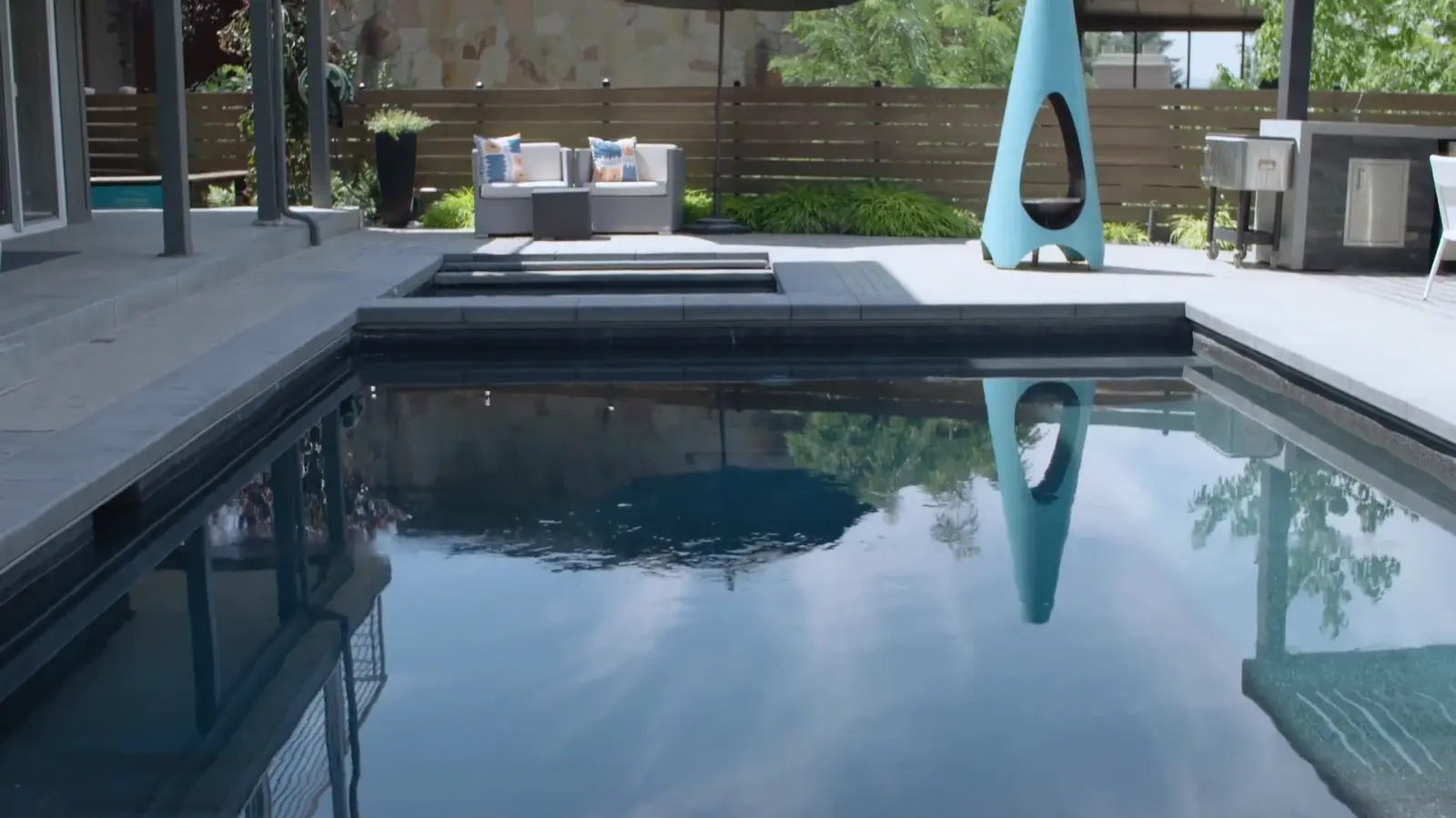 The finished Wallace Lane pool and spa, the teal fire feature reflected in the dark water